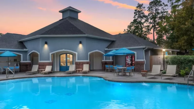 Inviting swimming pool at The Landings of Conroe at sunset, with a beautifully lit clubhouse, poolside seating, and vibrant blue sky with soft pink clouds.