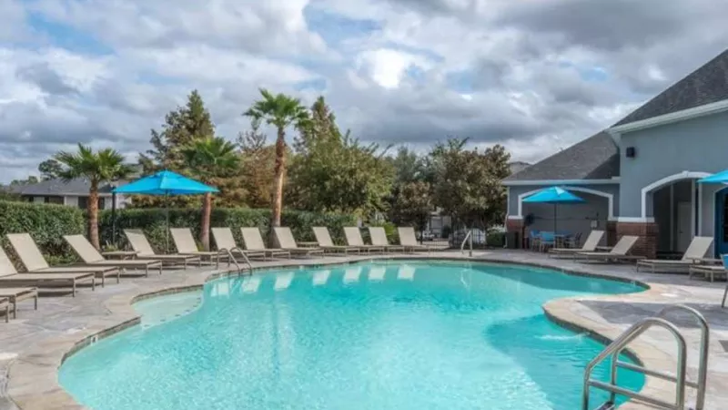 Sparkling blue pool with a stone-accented deck at The Landings of Conroe, featuring comfortable lounge chairs and shaded seating areas for relaxation.