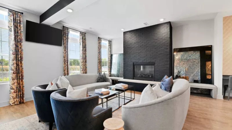 A contemporary social lounge with curved sofas, navy accent chairs, a sleek fireplace, and floor-to-ceiling windows.