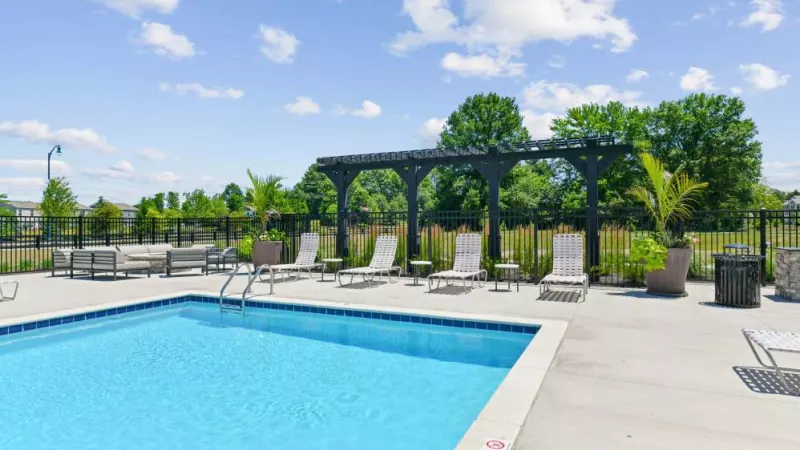 A resort-style pool surrounded by comfortable loungers, lush greenery, and a pergola offering shade.
