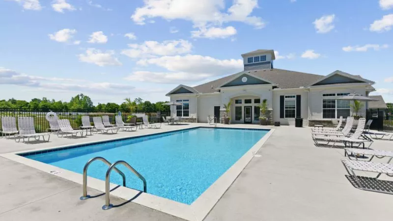 A crystal-clear pool surrounded by lounge chairs and palm trees, set against a backdrop of lush greenery and open sky.