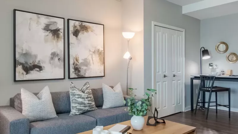 Modern living room with a gray sofa, abstract artwork, and a cozy workspace in the corner.