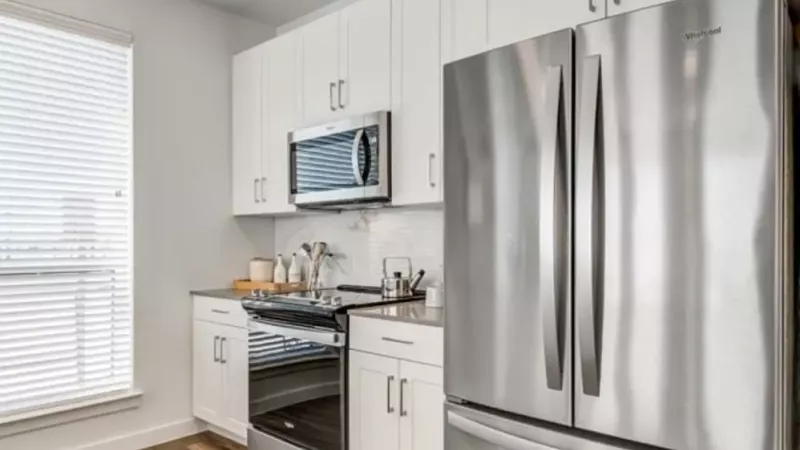 A modern kitchen featuring white cabinetry, stainless steel appliances, and a sleek wood floor.