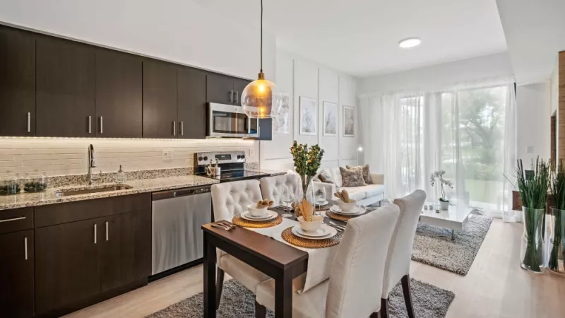 A sleek open-concept kitchen and living space with dark wood cabinetry, stainless steel appliances, and a stylish dining area with elegant pendant lighting.