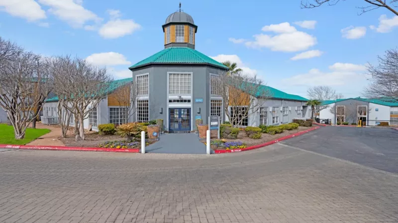 The Clara Apartments clubhouse with a distinctive teal roof and landscaped entrance.