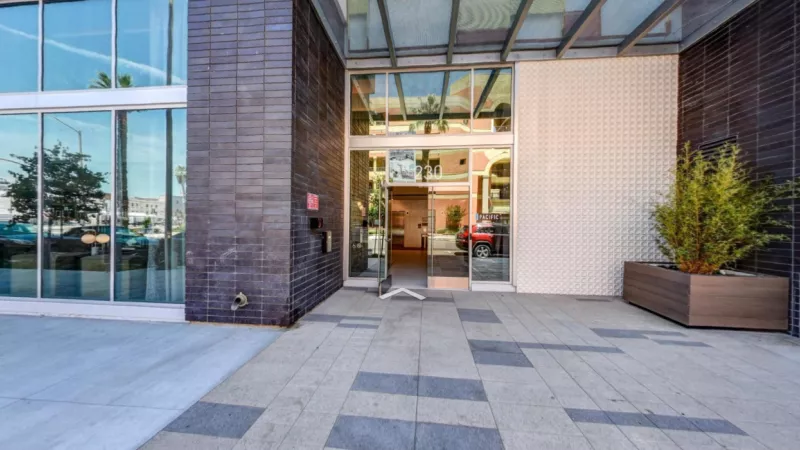 "Modern entrance of The Pacific Luxury Apartments featuring sleek glass doors, contemporary architecture, and landscaped greenery, offering a welcoming first impression."