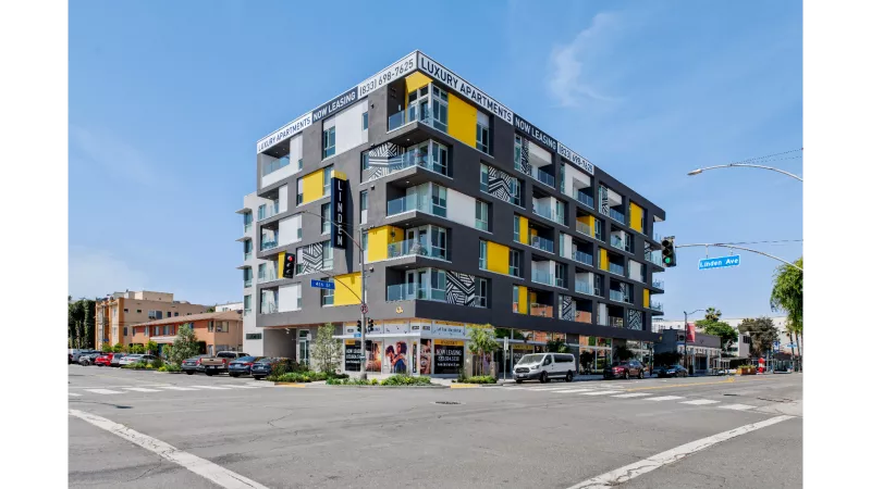 Modern exterior view of The Linden Luxury Apartments, featuring bold architecture with yellow and grey accents, spacious balconies, and prominent "Now Leasing" signage at the corner of 4th Street and Linden Avenue.