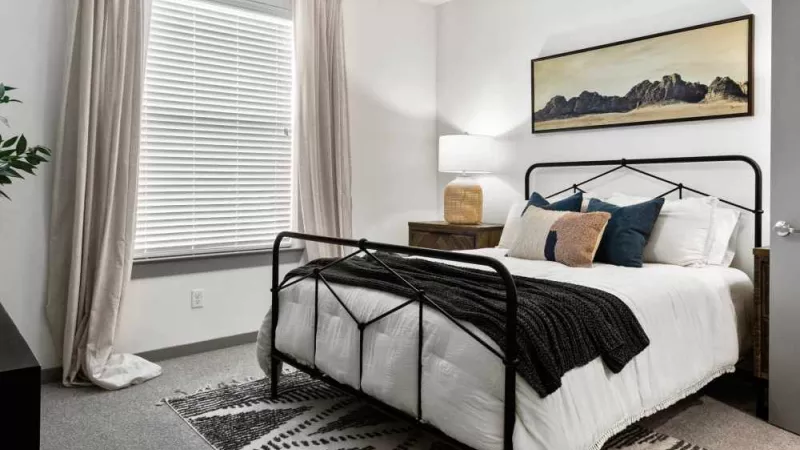 A serene bedroom with a modern metal bed frame, cozy bedding, and a large window for natural light.