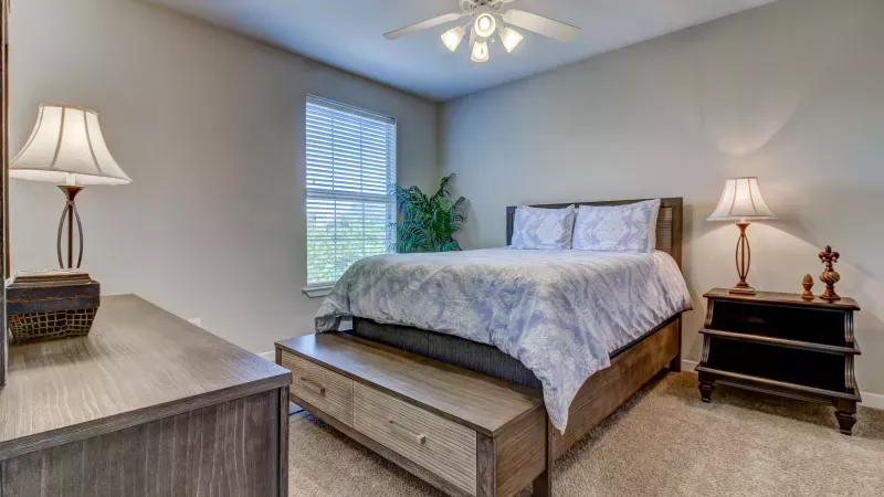 Comfortable bedroom with ceiling fan, natural light, and plush carpeting at The Saulet Apartments in New Orleans.