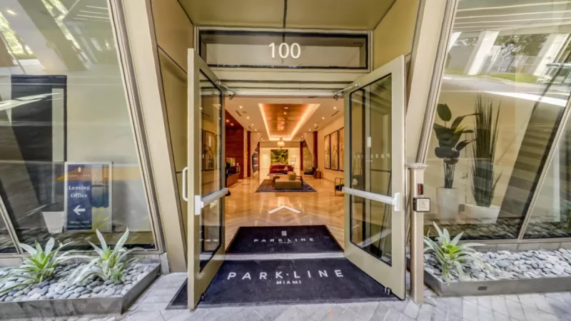 Main entrance of ParkLine Miami apartments with glass double doors leading into a bright lobby featuring modern seating, warm lighting, and contemporary décor.