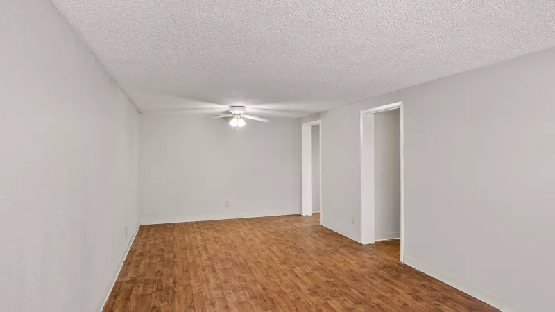 Empty living room with light gray walls, dark wood-look laminate floor, and a white ceiling fan.