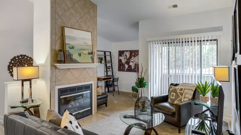 Spacious living room with a tiled fireplace, painting on mantel, dark sofa, glass tables, and a large sliding door.