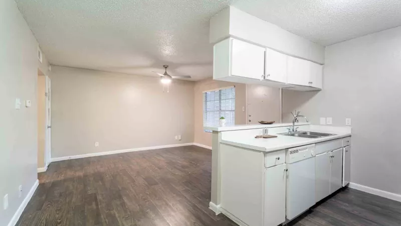 Modern unfurnished apartment with dark plank flooring, light beige walls, and a white kitchen with a sink and cabinets.