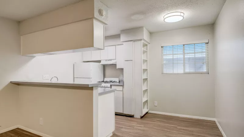 Clean, compact kitchen with white cabinets, appliances, a breakfast bar, wood-look floor, and a bright window.