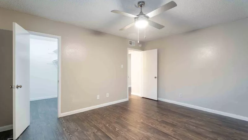 Unfurnished bedroom with light tan walls, dark laminate flooring, ceiling fan, and two open white doors.