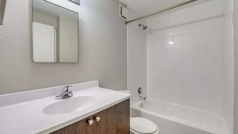 Clean bathroom with white tub, toilet, and dark wood vanity with sink and mirror.
