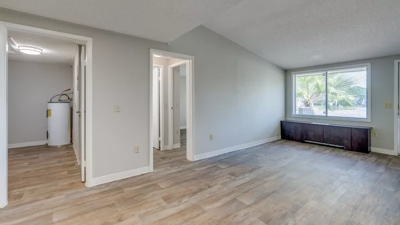 Spacious room with wood-look floor, light grey walls, a window bench, and a water heater visible through a doorway.