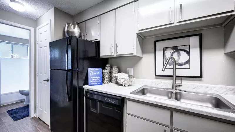 Modern kitchen with light grey cabinets, white speckled counters, black appliances, stainless steel sink, and abstract art.