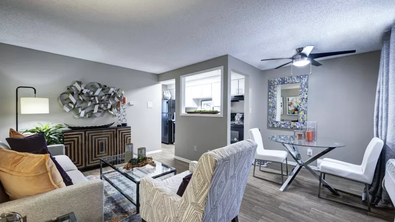 Bright living and dining area with a grey sofa, metallic wall art, and a glass dining table with a decorative mirror.