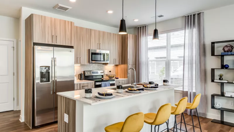 Modern kitchen with light wood cabinets, stainless steel appliances, a white island, and three yellow bar stools.