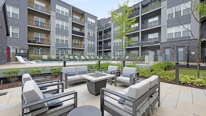 Modern apartment complex courtyard with grey patio furniture around a fire pit and a swimming pool in the background.
