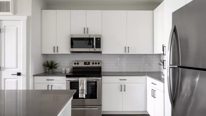 Modern kitchen with white cabinets, stainless steel oven, microwave, refrigerator, gray counter, and subway tile.