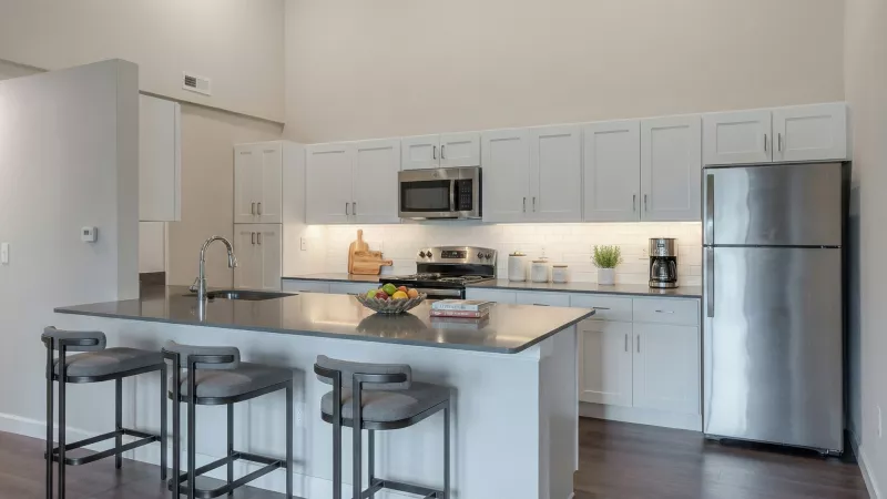 Modern kitchen with white cabinets, stainless steel appliances, a dark island with three bar stools, and a fruit bowl.