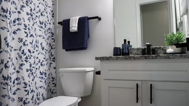 Blue floral shower curtain, white toilet, and modern bathroom vanity with granite countertop and mirror.