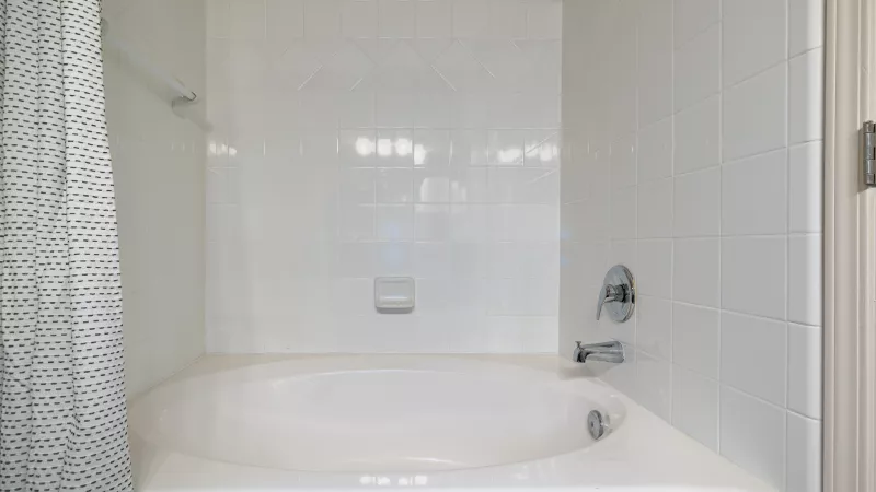White built-in bathtub in a tiled bathroom, with a shower curtain and chrome fixtures.