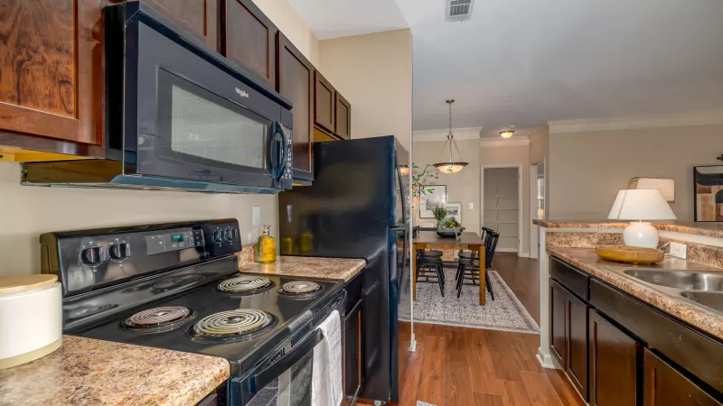 Modern kitchen with dark wood cabinets, black appliances, granite-patterned countertops, and a dining area beyond.