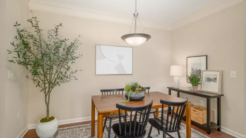 A modern dining room features a wooden table with black chairs, a chandelier, a large potted plant, and wall art.