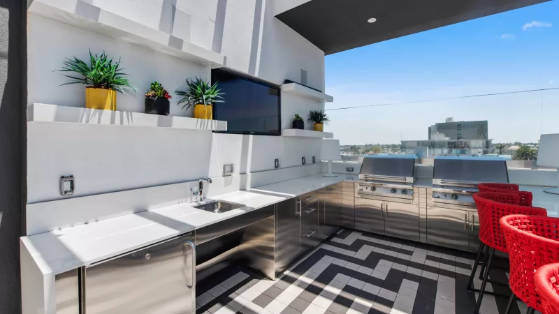 Modern rooftop outdoor kitchen with stainless steel appliances, white counters, red stools, and a chevron floor.