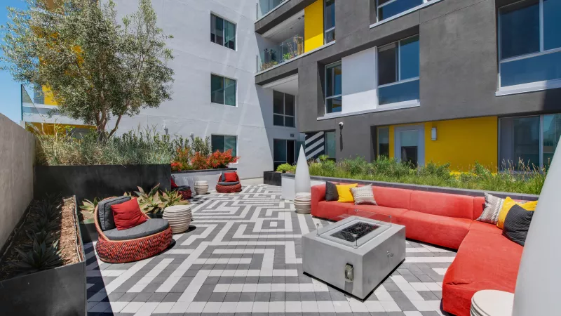 Modern outdoor patio with red seating, a fire pit, and a grey and white patterned floor, surrounded by a contemporary building.