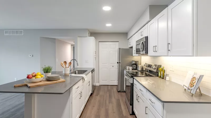 Modern kitchen with white cabinets, gray counters, a large island, stainless steel appliances, and wood floors.