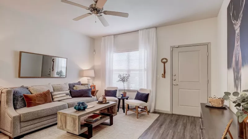 Bright living room featuring a beige sofa, wooden coffee table, two white armchairs, and a large deer print.