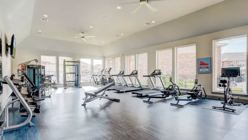 Modern fitness center with treadmills, ellipticals, weight machines, and large windows. Blue and grey floor.
