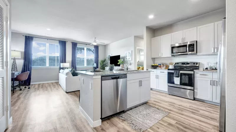 Open concept living room and kitchen featuring white cabinets, stainless steel appliances, a gray island, and blue curtains.