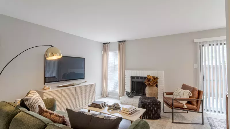 Bright living room featuring an olive green sofa, large TV, white fireplace with fall decor, and a brown leather armchair.