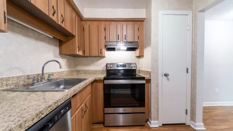 Kitchen with light brown cabinets, speckled countertops, stainless steel appliances including a range and sink, and wood floor.