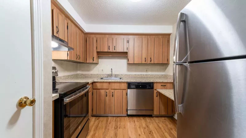 Clean kitchen with light wood cabinets, stainless steel appliances, and a wood floor. Refrigerator on right.