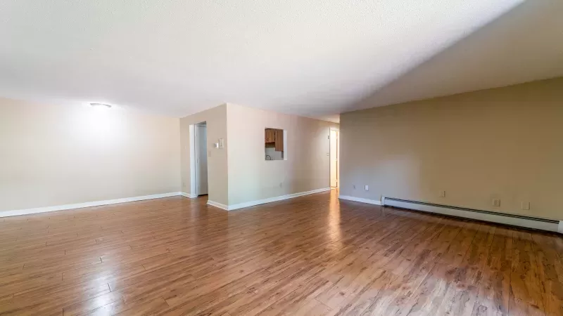 Spacious, empty room with light beige walls, wooden floor, and two doorways.