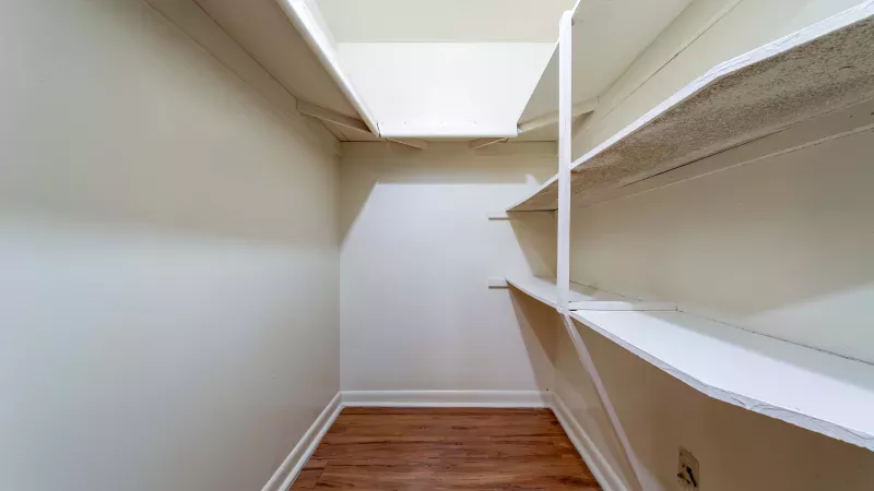 Empty white walk-in closet with brown wood floor and multiple shelves.