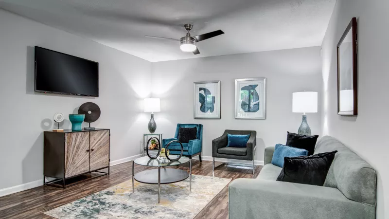 Contemporary living room with a light gray sofa, teal and dark gray armchairs, wood floor, patterned rug, TV, and modern decor.