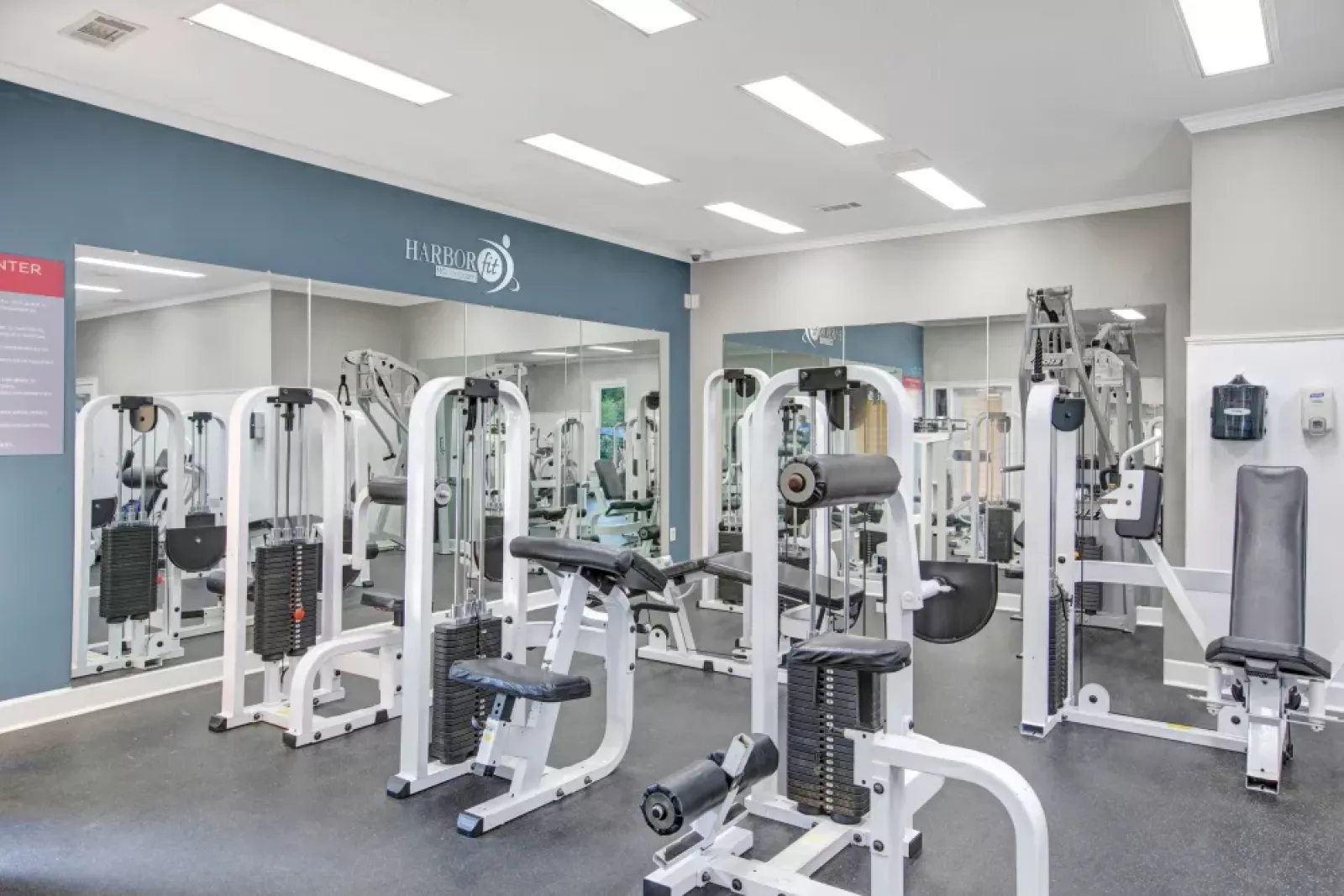A fully equipped fitness center featuring various strength training machines, a wall of mirrors for added functionality, and bright, modern lighting to create an inviting workout environment.