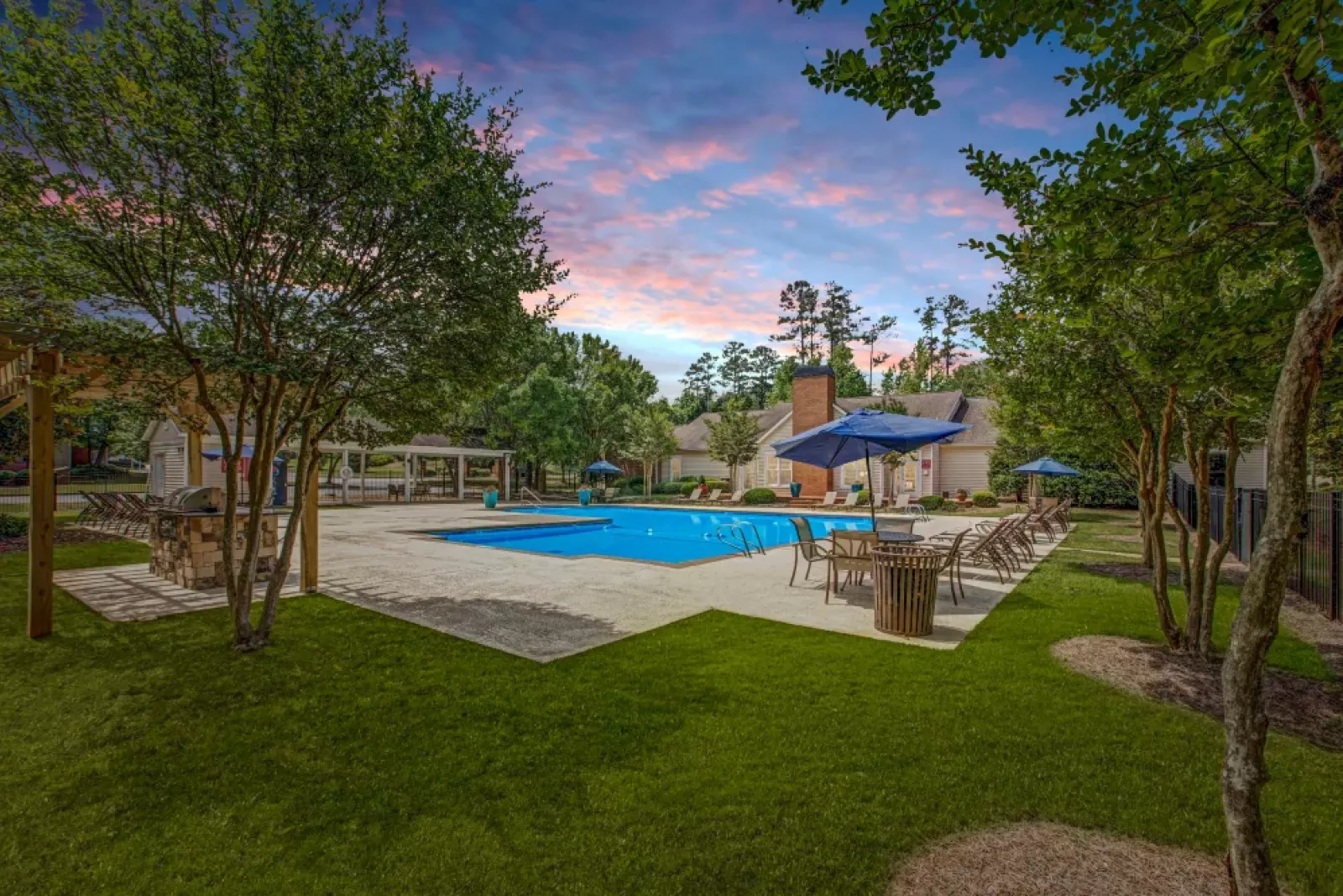 A wide view of the outdoor pool surrounded by lounge seating, lush greenery, and blue skies.