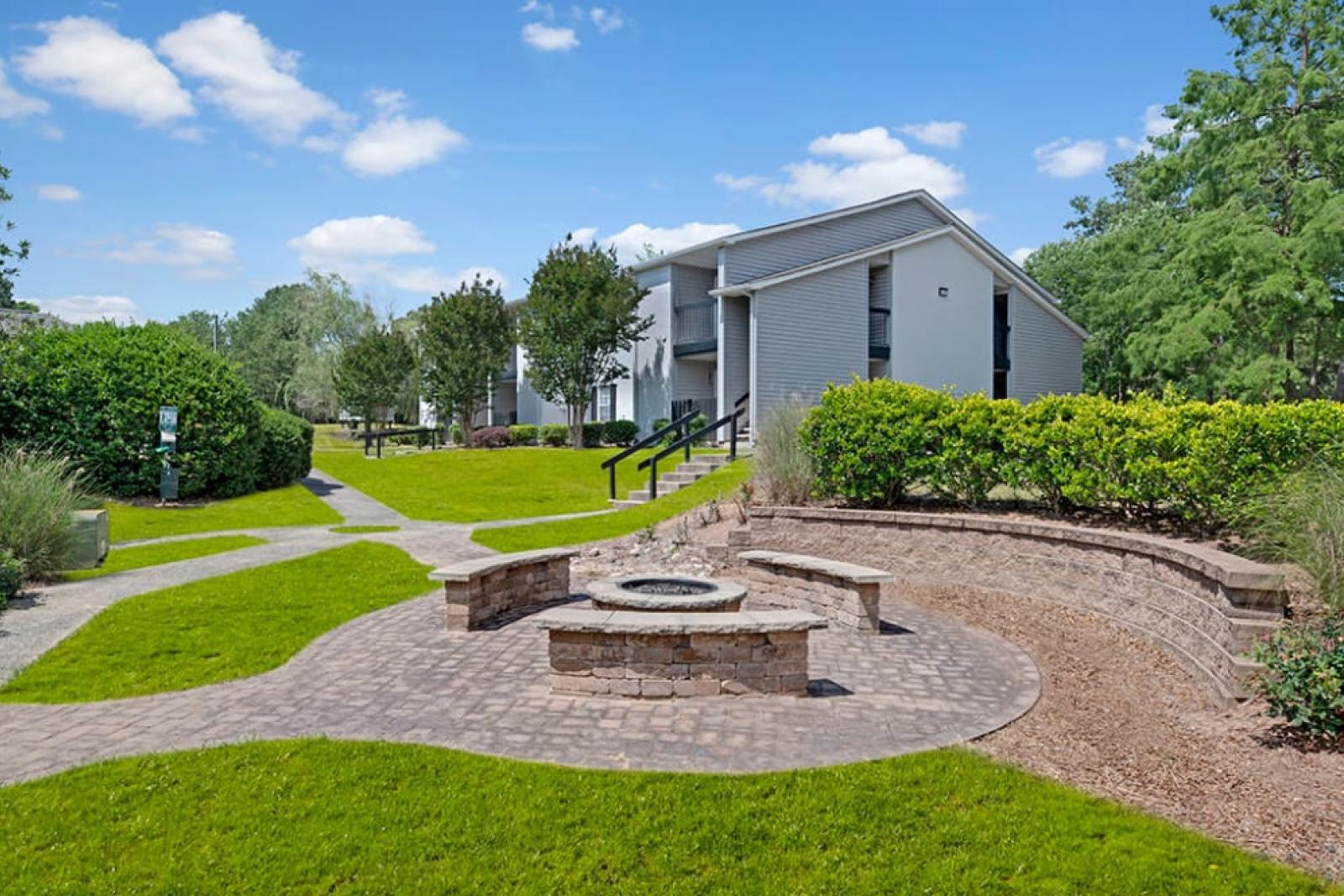 A building with a fountain in front, surrounded by grass and landscaping, with trees and a clear sky above.