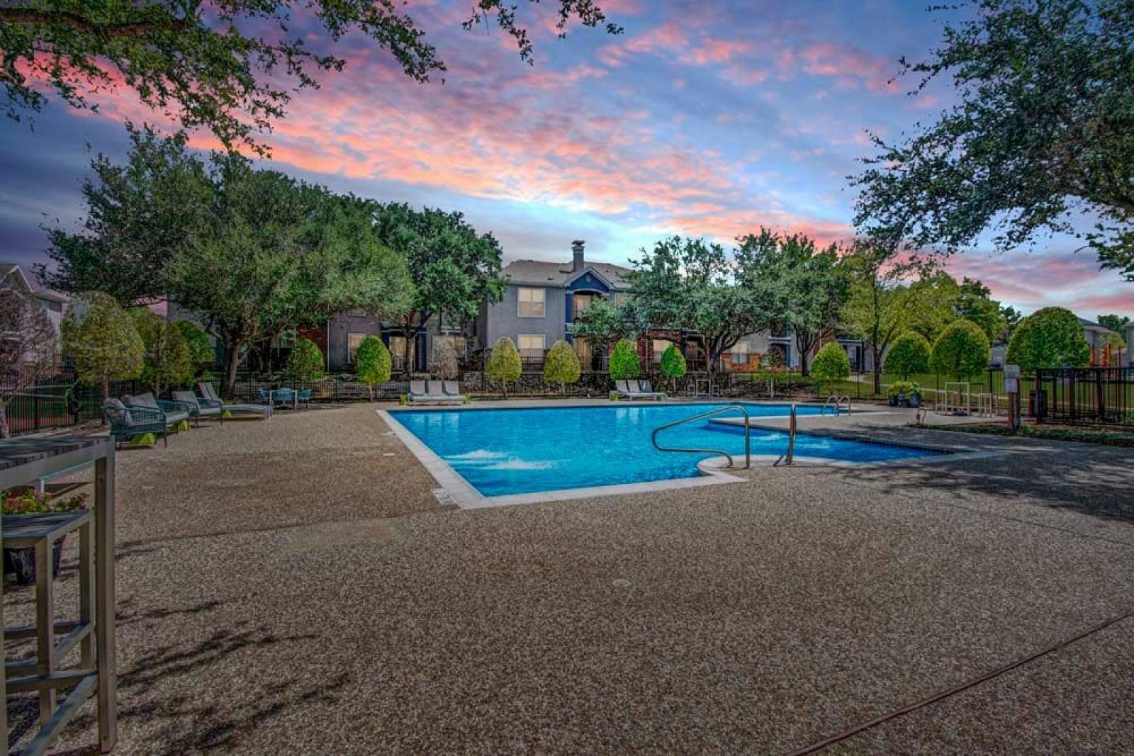 Stunning community pool captured at sunset, with vibrant skies reflecting on the water. The well-lit space offers a serene evening ambiance for relaxation or a refreshing swim.