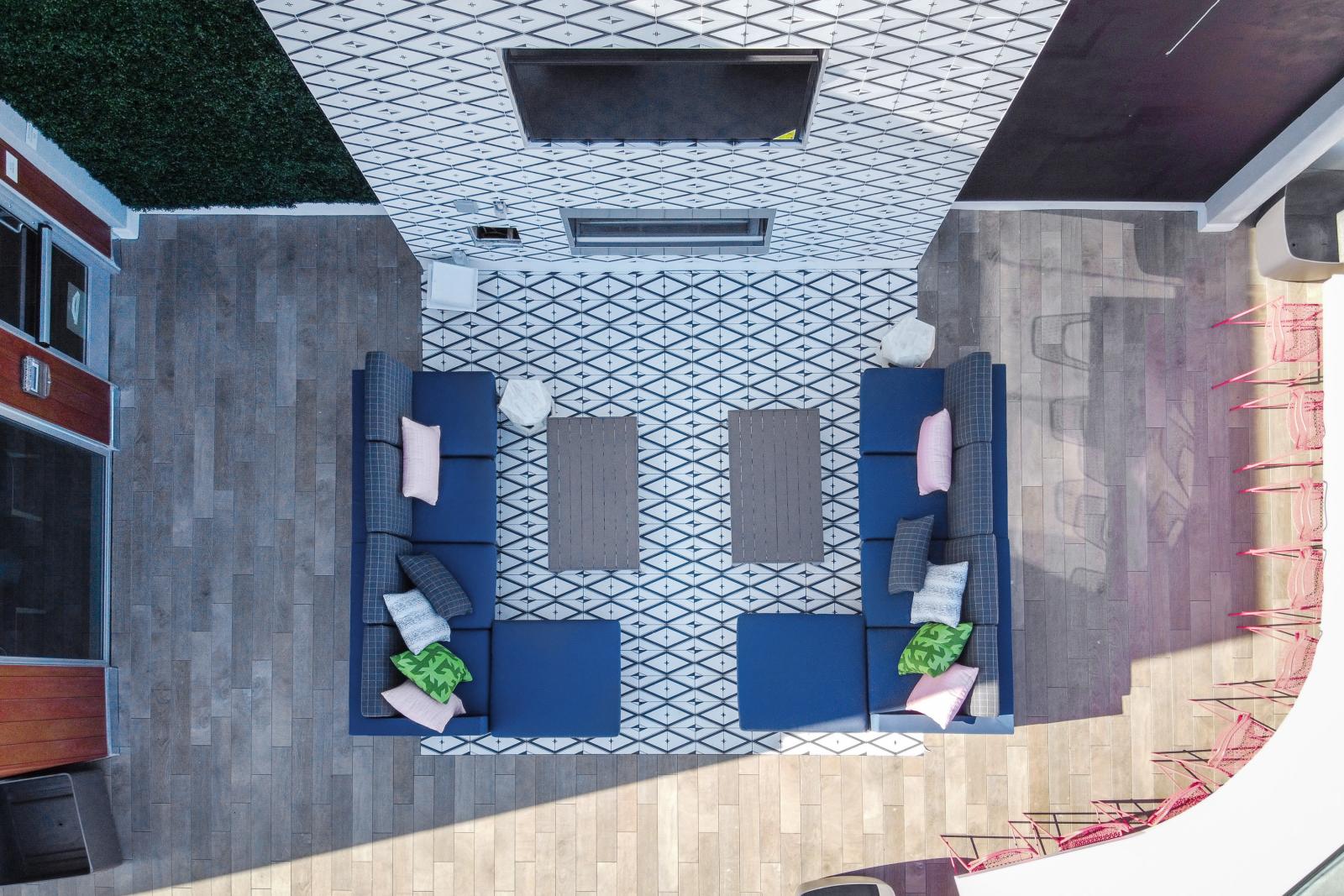 Modern outdoor lounge with blue sofas, colorful cushions, geometric tiles, and a wall-mounted TV.