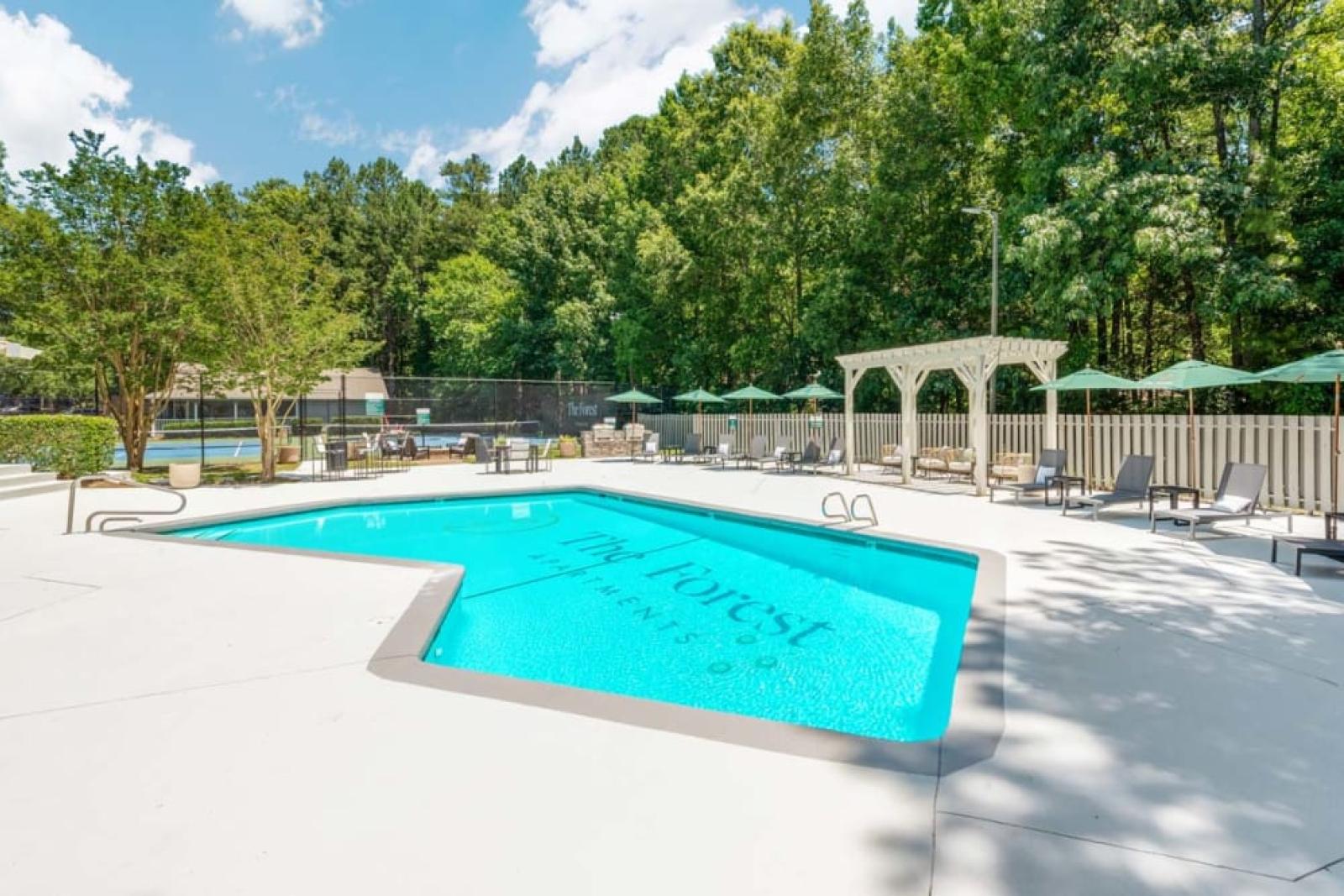 A refreshing outdoor pool with "The Forest Apartments" branding, surrounded by lush greenery and lounge chairs.