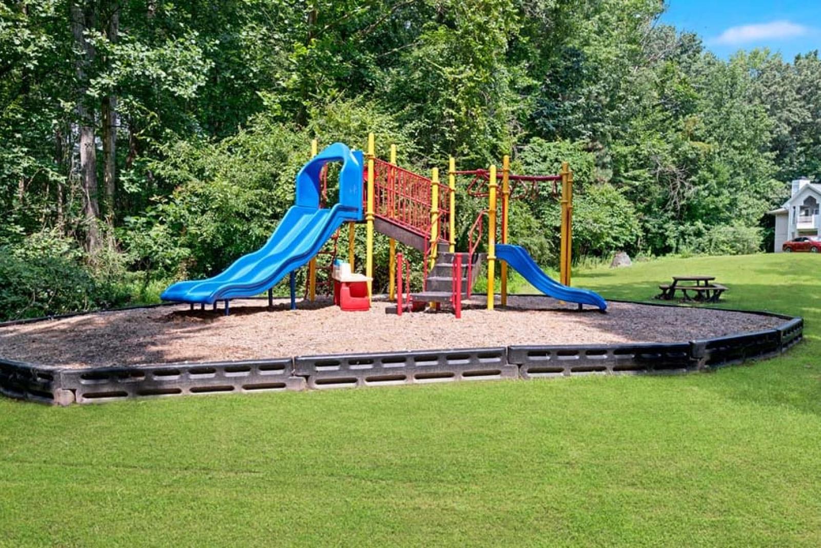 A children's playground with colorful slides and swings surrounded by greenery.